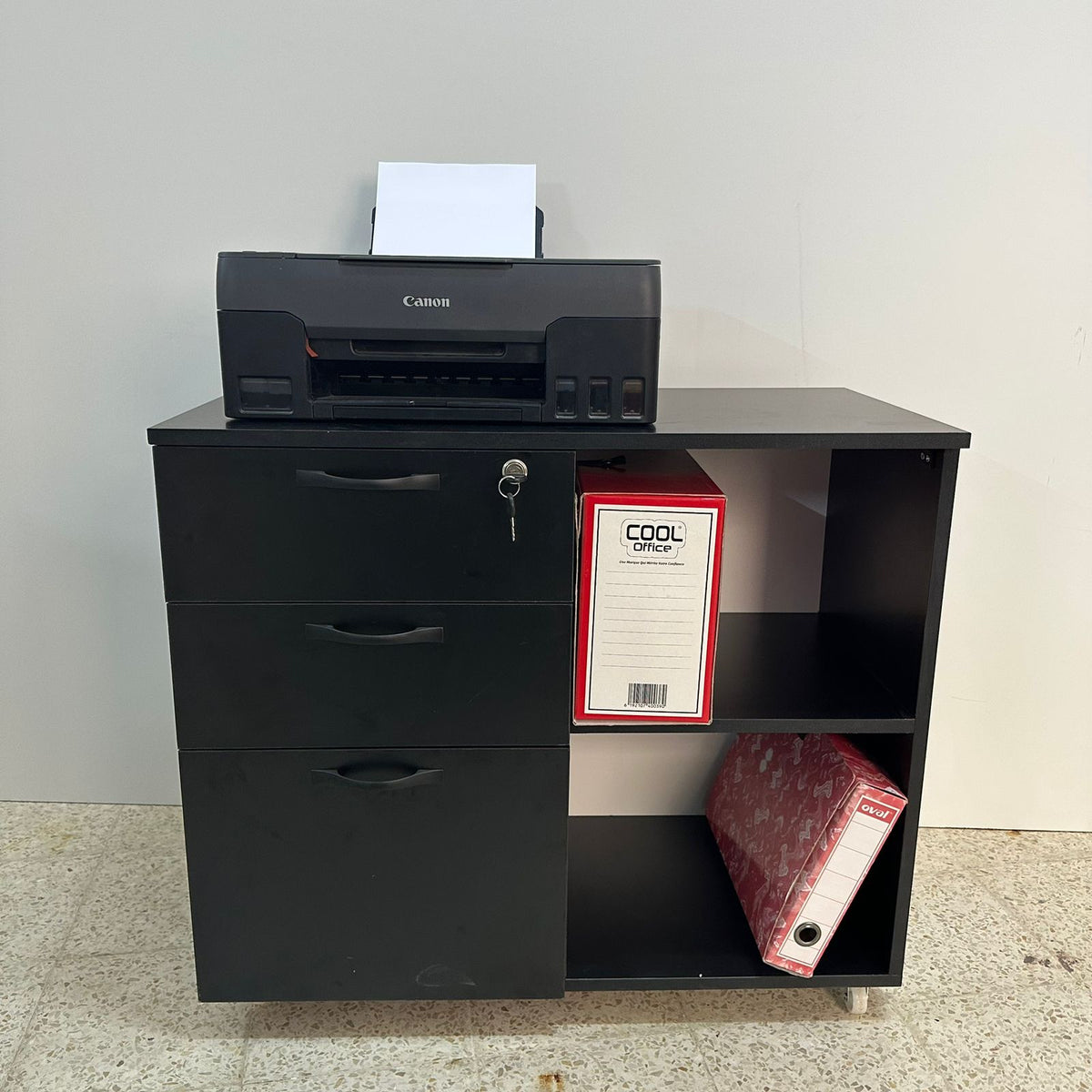Meuble rangement bureau noir – vue frontale avec imprimante Canon et classeurs, roulettes visibles
